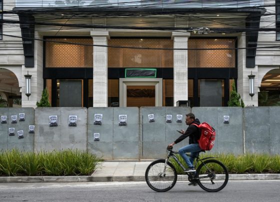 A man rides his bike past the facade of the Banco Master protected by hoardings, with the bank's logo covered in plastic, in Sao Paulo, Brazil, on January 22, 2026, after Brazil's Central Bank ordered its shutdown due to a major liquidity crunch and "serious violations" of financial regulations. (Photo by NELSON ALMEIDA / AFP)